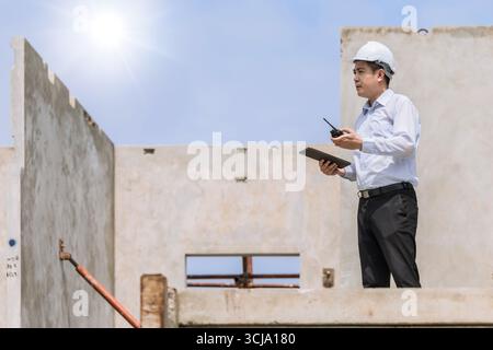 Asian engineer overseeing construction project at urban site professional environment high angle viewpoint Stock Photo