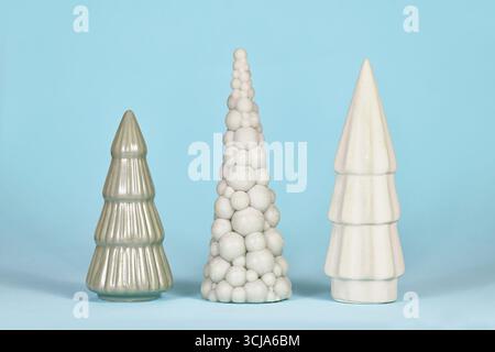 Three different shaped light green ceramic Christmas trees on blue background Stock Photo