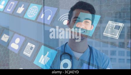 Standing male doctor wearing scrubs and stethoscope using digital icons on glass window in clinic Stock Photo