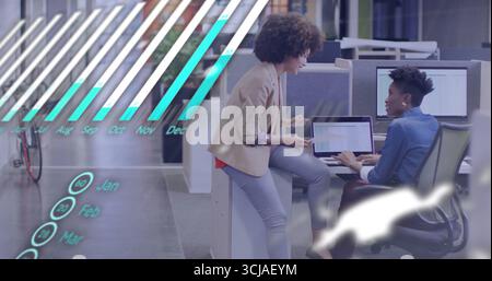 Collaborating two women in business attire analyzing charts on laptop in office with data overlays Stock Photo