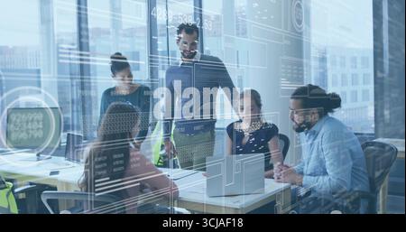 Discussing group of developers examining laptops in office with glass partitions and code overlays Stock Photo