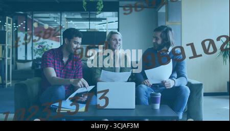 Collaborating professionals reviewing documents on laptop in office lounge on sofa, with coffee cup Stock Photo