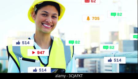 Smiling engineer wearing hard hat, vest, holding tablet on rooftop terrace, with notification icons Stock Photo