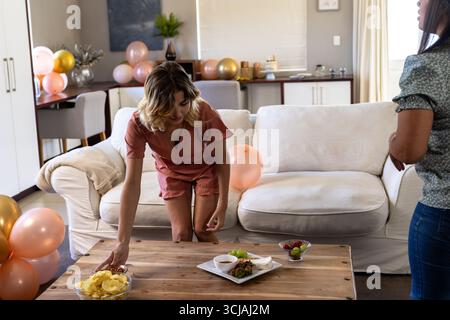 Woman arranging snacks on table in living room, preparing for celebration Stock Photo