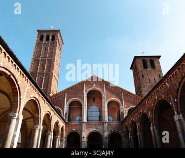Basilica di Sant’Ambrogio with Romanesque architecture, twin bell towers, and brick arches under clear blue sky. Stock Photo