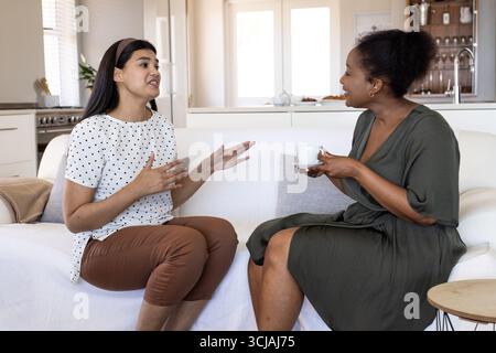 Two women sitting on sofa at home, enjoying coffee and having conversation Stock Photo