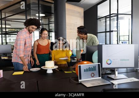 Celebrating at office, diverse colleagues enjoying cake and conversation around desk Stock Photo