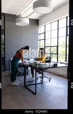Two women collaborating at office desk, reviewing documents in modern workspace Stock Photo