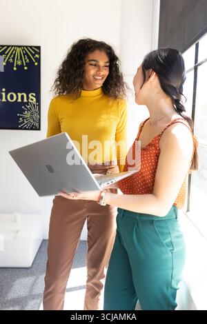 Two businesswomen discussing project while holding laptop in modern office Stock Photo