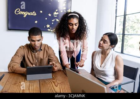 Team collaborating on digital tablets in modern office, discussing project details Stock Photo