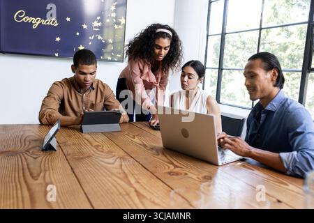 Diverse business team collaborating on digital devices in modern office meeting Stock Photo