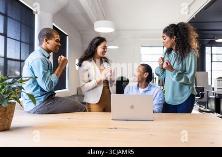 Diverse business team collaborating around laptop in modern office, sharing ideas Stock Photo