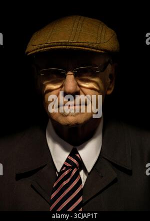 A portrait of an older man wearing a tweed cap, glasses, a suit, and a tie. The man is looking directly at the camera. Stock Photo