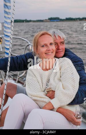 Elderly couple sharing a joyful moment on a sailboat, embracing each other with nature and water in the background, radiating elegance and happiness Stock Photo