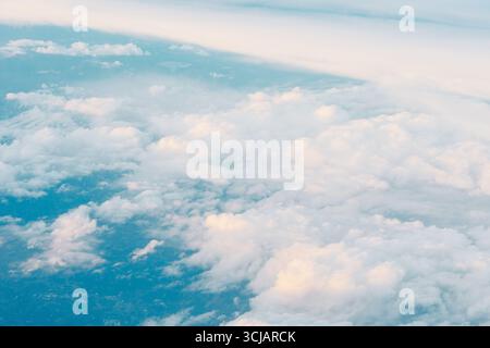Aerial shot looking down at a vast expanse of clouds. Clouds appear fluffy and white, with some casting soft shadows on the blue sky below Stock Photo