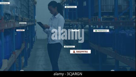 Analyzing clerk wearing uniform reviewing stock levels on tablet in warehouse aisle, with blue bins Stock Photo