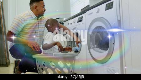 Kneeling father-son duo loading clothes from plastic basket into washer in laundry room, copy space Stock Photo