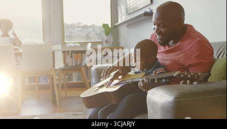 Playing father and son practicing chords in home living room, holding acoustic guitar, copy space Stock Photo