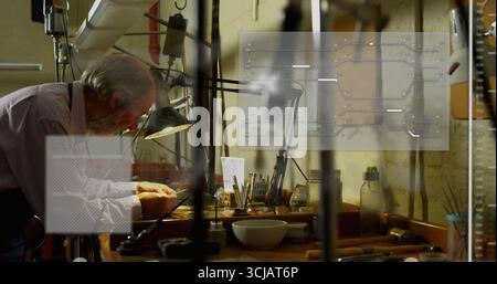 Examining senior craftsman in workshop leaning over workbench under lamp using tools, copy space Stock Photo