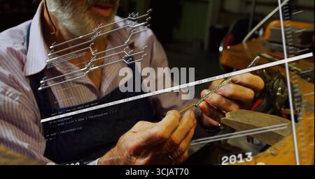 Craftsman holding metal part and filing edges at workbench with vise, wearing striped shirt, apron Stock Photo
