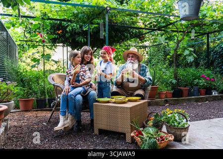 Farmers enjoying organic sandwiches during lunch break in a bio farm garden, surrounded by fresh vegetables and fruit plants, promoting healthy lifest Stock Photo