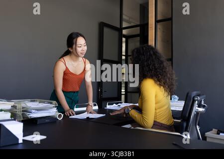 Two women discussing documents at office desk, collaborating on project Stock Photo