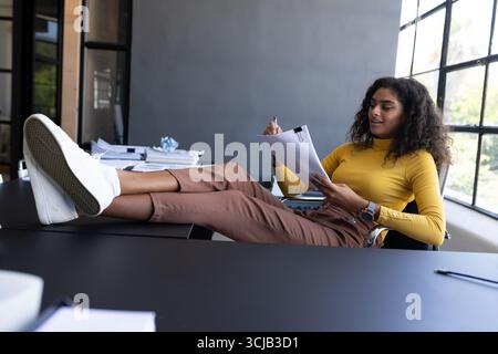 Relaxed businesswoman reviewing documents with feet up on office desk Stock Photo