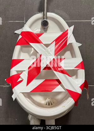 A toilet urinal with tape showing that the pumbing needs fixing or is out of use.  The cost to call out a plumber is an expensive business or domestic Stock Photo
