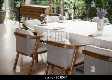 Empty table and chairs in a restaurant. Outdoor terrace with grey wooden chairs and table covered with white cloth. Stock Photo