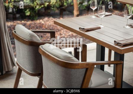 Empty outdoor table and chairs in a restaurant. Terrace with wooden chairs and table, bushes in garden int he background. Stock Photo