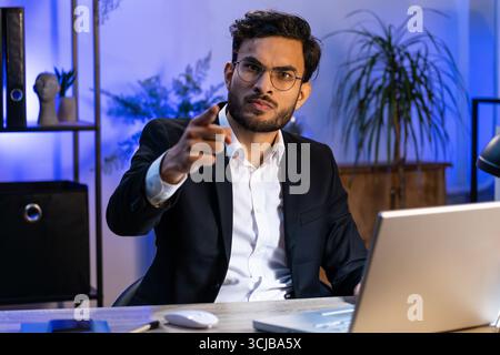 I choose you. Serious Indian businessman programmer software developer working on office laptop pointing to camera, looking with strict expression, making choice showing direction. Arab freelancer man Stock Photo