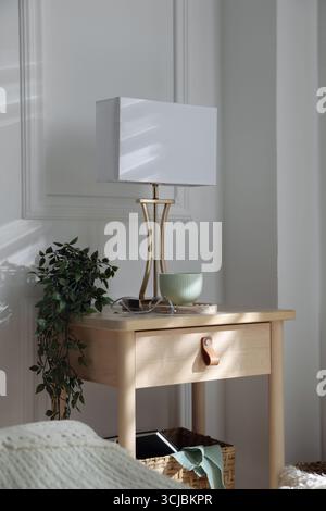 Bedside table with lamp and other decor near bed indoors Stock Photo
