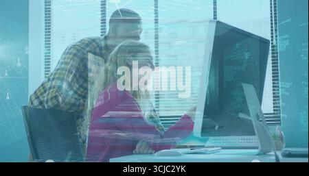 Collaborating engineers with pink blazer pointing at code on office monitor, with wireless keyboard Stock Photo