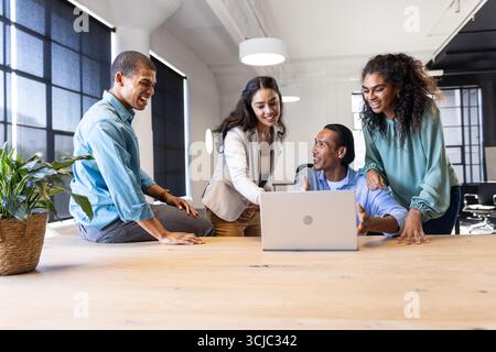 Diverse business team collaborating around laptop in modern office, sharing ideas Stock Photo