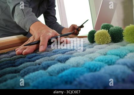 Close-up of interior designer’s hands choosing blue fabric swatches with a stylus. Color samples in textile palette showcase material textures for cre Stock Photo