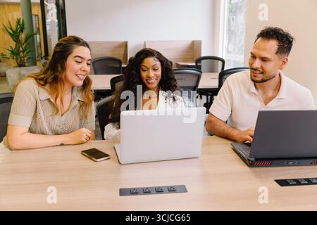 A diverse team of professionals collaborates in a modern coworking space. Engaged in discussion, they use laptops for brainstorming and planning in a Stock Photo