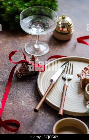 Elegant Christmas table setting featuring a festive gingerbread cookie with red ribbon, a glass, and a plate with cutlery. Ideal for holiday celebrati Stock Photo