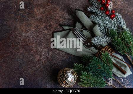 Elegant Christmas table setting featuring green napkins, silverware, and festive pine branches adorned with frosted tips. A touch of red berries adds Stock Photo