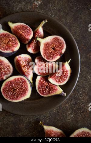 Top view of ripe, halved figs arranged on a dark brown plate against a textured, earthy background. The figs feature a rich, vibrant color, emphasizin Stock Photo