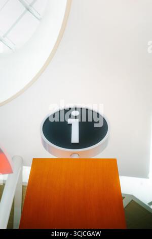 From below modern airport information sign within a sleek terminal. The sign features a bold i symbolizing information, set against a clean and contem Stock Photo
