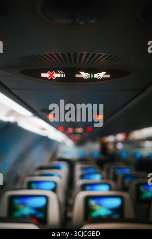 Close-up view of an airplane cabin interior showing illuminated safety signs above the seats, including no smoking and fasten seatbelt indicators, wit Stock Photo