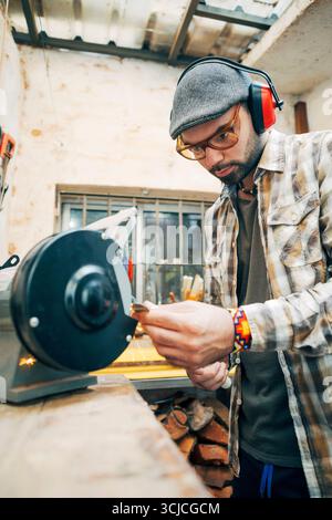 A skilled craftsman working meticulously at his workbench, wearing protective gear, as he shapes a flute. His focus on detail ensures the perfect soun Stock Photo