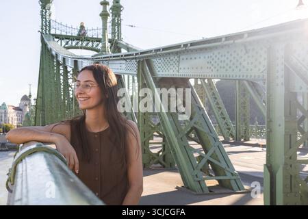 A woman with long hair smiles while standing on a historic bridge in Budapest, capturing the essence of a joyful travel experience in Europe under the Stock Photo
