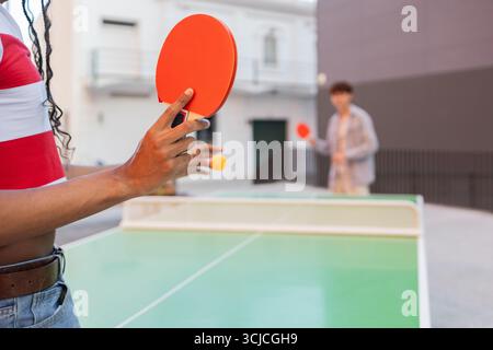 Cropped unrecognizable image of university students engaging in a friendly table tennis match outdoors, capturing the essence of student camaraderie a Stock Photo