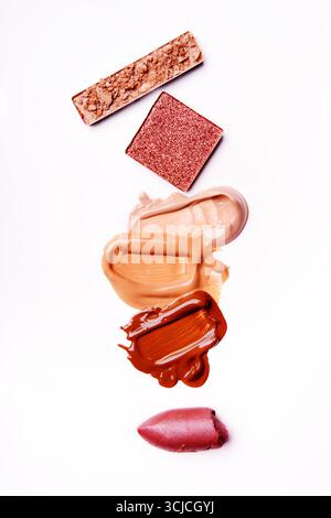 A captivating arrangement of broken eyeshadow, smeared foundations, and lipstick on a stark white background. This image highlights the textures and v Stock Photo