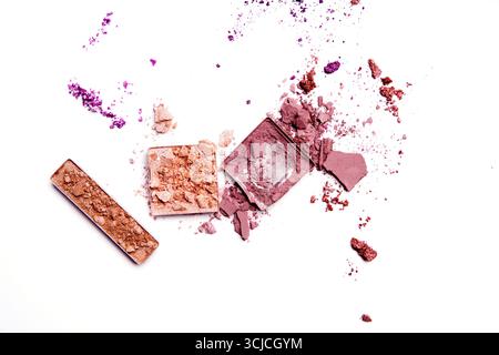 Close-up image of various broken eye shadows scattered on a white surface. The colors range from earthy browns to vibrant purples, depicting a makeup Stock Photo