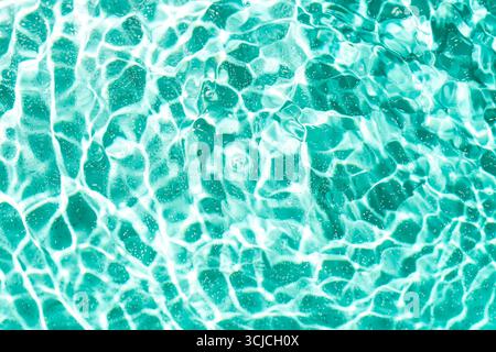 A close-up image of a pool's rippling turquoise water surface, capturing sunlight reflections that create a mesmerizing pattern. The texture is calmin Stock Photo