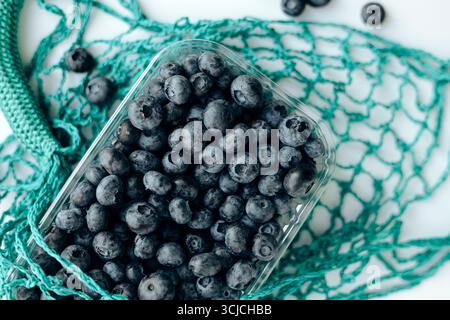 A top-down view of fresh blueberries in a transparent container placed on eco-friendly netting. The berries and sustainable packaging convey freshness Stock Photo