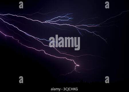 Intense lightning streaks illuminate a dark night sky, capturing the energetic power of a storm. The bright flashes create a stark contrast against th Stock Photo
