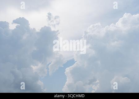 A beautiful image of majestic, fluffy clouds set against a pale blue sky, viewed from below. The contrasting light and shadows create a serene and dra Stock Photo